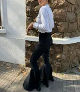 Pantalón negro de tiro alto con corte acampanado y terminación en volado en el ruedo.