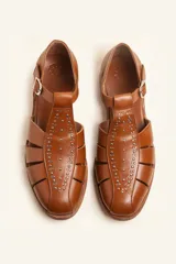 Sandalias de cuero color marrón, tipo romanas, con talón cerrado, tira en T con detalles de tachas metálicas, aberturas laterales y cierre de hebilla ajustable. Tienen tacón bajo de madera.
