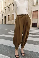 Pantalón de tiro medio con diseño bombacho, frunces delanteros y pierna abullonada con puños ajustados. Incluye bolsillos frontales y un cinturón decorativo con cadena metálica.