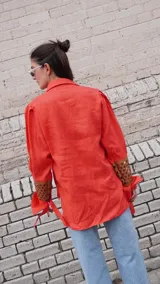 Camisa de lino color naranja, con mangas largas abuchonadas, cuello camisero y cierre frontal con botones. Presenta un diseño único con detalle calado en los puños.