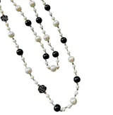 Collar largo estilo Chanel compuesto por una cadena dorada intercalada con perlas blancas, esferas negras y pequeños dijes de flores esmaltadas en blanco y negro.