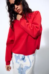 Sudadera de punto lisa en color rojo, con cuello subido y manga larga. Presenta un diseño de corte holgado con acabados en rib en puños y ruedo.