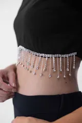 Top negro corto con mangas largas, cuello redondo y detalle de flecos de strass colgantes en el ruedo.