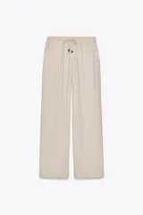 Pantalón negro de tiro alto con cintura elástica ajustable mediante cordones con terminales dorados. Presenta pernera ancha y bolsillos laterales. La tela tiene una textura sutilmente arrugada o plisada.