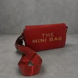 Cartera tipo bandolera de tamaño pequeño, color rojo, con solapa frontal y letras doradas estampadas que dicen 'THE MINI BAG'. Incluye una correa de tela ajustable y herrajes metálicos.