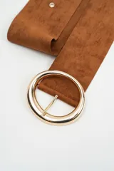 Cinturón ancho de gamuza color marrón, con hebilla circular grande de metal dorado y ojales metálicos a lo largo de la tira.