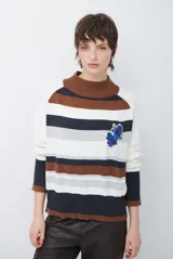 Polera de tejido de punto con diseño de rayas horizontales en tonos beige, marrón, gris y negro. Presenta cuello redondo y mangas largas con puños en contraste.