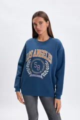 Buzo de algodón azul con cuello redondo, corte oversize y diseño bordado frontal con estilo universitario que incluye el texto Los Angeles y el número 58.