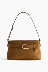 Cartera de hombro color tostado con acabado de gamuza, correa ajustable y tira decorativa frontal con hebilla metálica dorada.