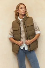 Chaleco puffer color crema, con cuello alto, cierre frontal y cuatro bolsillos con solapa. Cuenta con cintura ajustable con cordón.