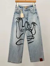 Jean de corte wide leg en denim azul claro, intervenido a mano con ilustraciones abstractas de rostros en líneas color rosa y blanco. Presenta tiro medio-alto y diseño de cinco bolsillos.