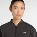 Campera tipo bomber de New Balance, color gris oscuro, con cierre frontal completo, cuello, puños y ruedo acanalados. Presenta bolsillos laterales y el logo de la marca bordado en el pecho.