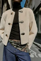 Chaqueta de cuello redondo y manga larga con tejido exterior efecto pelo e interior efecto ante. Presenta bolsillos delanteros de vivo y cierre frontal con alamares metálicos.