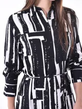 Vestido camisero midi de manga larga, con cuello y botones frontales, ajustado a la cintura con un lazo. Presenta un estampado abstracto en tonos azul claro y azul oscuro/negro.