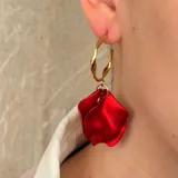 Aros de tipo argolla dorada con diseño retorcido, de los cuales cuelga un dije en forma de pétalo de flor en color rojo vibrante.