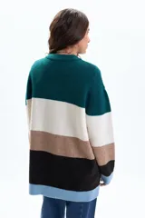 Buzo de tejido de punto con diseño de franjas horizontales en bloques de color verde, blanco, marrón, negro y celeste. Presenta cuello redondo, mangas largas y un corte holgado.