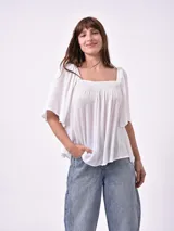 Blusa blanca de manga corta con escote cuadrado y fruncido en el busto. La tela parece tener textura plisada o arrugada.