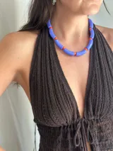 Collar corto compuesto por cuentas tubulares acrílicas de color azul lavanda y cuentas pequeñas esféricas de color naranja.