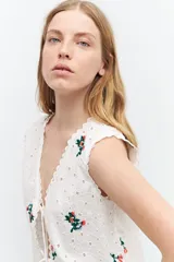 Chaleco blanco de broderie con bordados florales, escote en V y cierre con lazos.