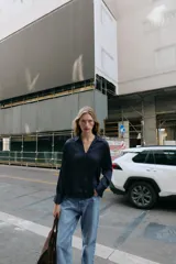 Camisa de cuello solapa y manga larga, confeccionada en tejido satinado azul marino. Presenta cierre frontal con botones forrados a tono y puños rectos.