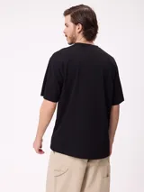 Remera negra de corte holgado con pequeño logo bordado en el pecho que incluye un diseño de pez y la marca Rusty.