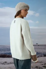 Cardigan tejido de punto en color natural, con cuello redondo, cierre frontal de botones oscuros y dos bolsillos delanteros. Presenta mangas largas con puños acanalados.