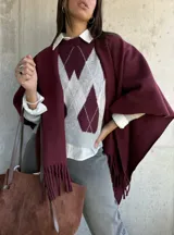 Ruana de tejido de punto en color bordó, con diseño abierto y terminación de flecos en los bordes.