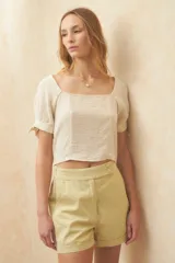 Top corto color blanco roto, con escote cuadrado, manga corta abullonada con lazos ajustables en el borde y textura arrugada en el tejido.