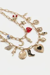Collar doble de cadena dorada con múltiples dijes colgantes, incluyendo corazones, estrella, símbolo de la paz, cerezas y lunas.