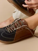 Championes de cuero con diseño tricolor en tonos negro, marrón y crema. Presentan cordones trenzados, costuras a la vista y detalle de pespuntes en el talón.