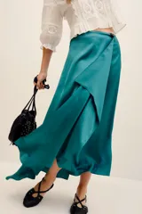 Falda cruzada satinada color verde, con caída irregular y diseño largo con movimiento. Incluye un pin decorativo de flor con perlitas.