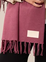 Pashmina de textura suave y color crema, con diseño liso y terminaciones en flecos en los extremos. Incluye una etiqueta decorativa en una de las esquinas.