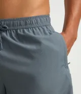 Bermuda deportiva masculina de color gris azulado, confeccionada en tejido técnico con textura perforada. Presenta cintura elástica con cordón de ajuste y diseño funcional para entrenamiento.