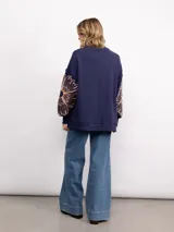 Buzo de algodón color negro con cuello redondo, mangas largas y bordado floral XL en color cobre en las mangas. Presenta un diseño holgado y cómodo.