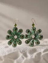 Aros colgantes con diseño de flor de ocho pétalos en cobre oxidado con acabado de pátina verde y detalles de tachas doradas. Incluyen un cristal verde en la parte superior y pasante de plata esterlina.