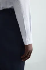 Camisa de manga larga para hombre, corte slim fit, con cuello italiano y cierre frontal de botonadura. Presenta un microestampado de cuadros pequeños en tonos blanco y celeste.