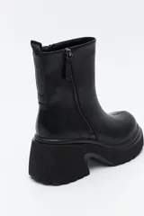 Bota de caña media color negro, con plataforma robusta y suela dentada. Presenta un diseño minimalista con cierre lateral para un calce práctico.