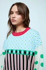 Sweater de punto con diseño geométrico y a rayas, de corte holgado y manga larga. Presenta un patrón combinado de lunares en las mangas, rombos en la parte superior y rayas verticales en el cuerpo.