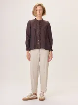 Camisa de lino rústico color marrón oscuro, con cuello mao, botones frontales y detalles de volados en el frente. Mangas largas con puños fruncidos.