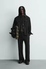 Sobrecamisa de corte relajado confeccionada en tejido efecto piel color marrón oscuro. Presenta cuello solapa, cierre frontal con botones metálicos, mangas largas con puños abotonados y dos bolsillos de plastrón con solapa en el pecho.