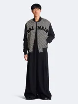 Campera Balmain estilo varsity con estampado monogrammed en blanco y negro, mangas largas negras y cierre frontal con botones a presión.