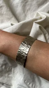 Pulsera brazalete rígido de alpaca plateada con textura irregular hecha a mano.