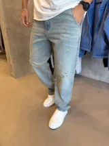 Jean de corte mom con efecto desgastado y roturas localizadas en las piernas. Presenta un tono azul claro lavado, cierre frontal con botón y bolsillos laterales.