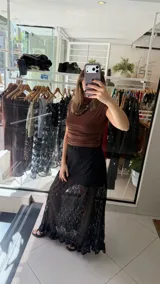 Falda larga de encaje negro con diseño de capas, presentando una sección superior opaca y una sección inferior transparente con terminación de volado en el ruedo.