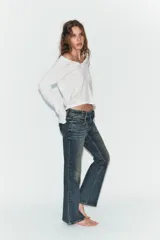 Jeans de tiro bajo con corte bootcut, confeccionados en denim con efecto lavado. Presentan costuras verticales marcadas en el frente, cierre frontal con cremallera, gancho metálico y detalle de trabilla con botones en la cintura.