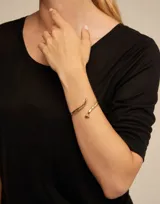 Pulsera abierta de diseño minimalista con acabado en plata, inspirada en la forma de un clavo con detalle de resorte central y grabado de la marca.