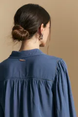 Camisa de manga larga color celeste, con cuello clásico, cierre frontal con botones y puños elastizados con volados. Presenta un diseño fluido con detalle de vainilla en la espalda.