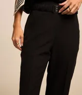 Pantalón de corte recto para mujer, confeccionado en jacquard negro con textura. Cuenta con cintura elástica integrada, hebilla decorativa frontal y cierre lateral.