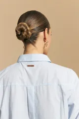 Camisa de corte clásico y holgado, confeccionada en tela blanca, con cuello camisero, cierre frontal de botones de nácar y mangas largas con puños abotonados.