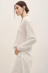 Camisa de manga larga blanca con detalles de encaje y entredos verticales, escote en V y cuello mao con volados sutiles.